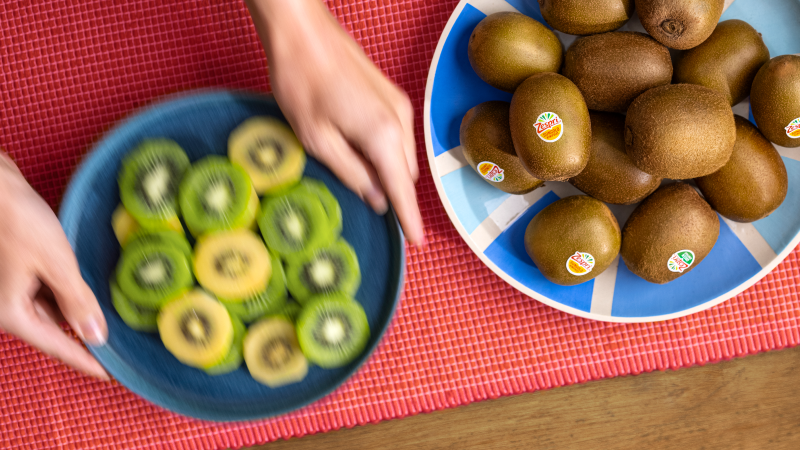 A bowl of whole kiwifruit beside a bowl of sliced and peeled Green and SunGold kiwifruit on a red tablecloth